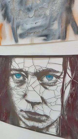 A cracked artwork of a woman's face is displayed on a wall